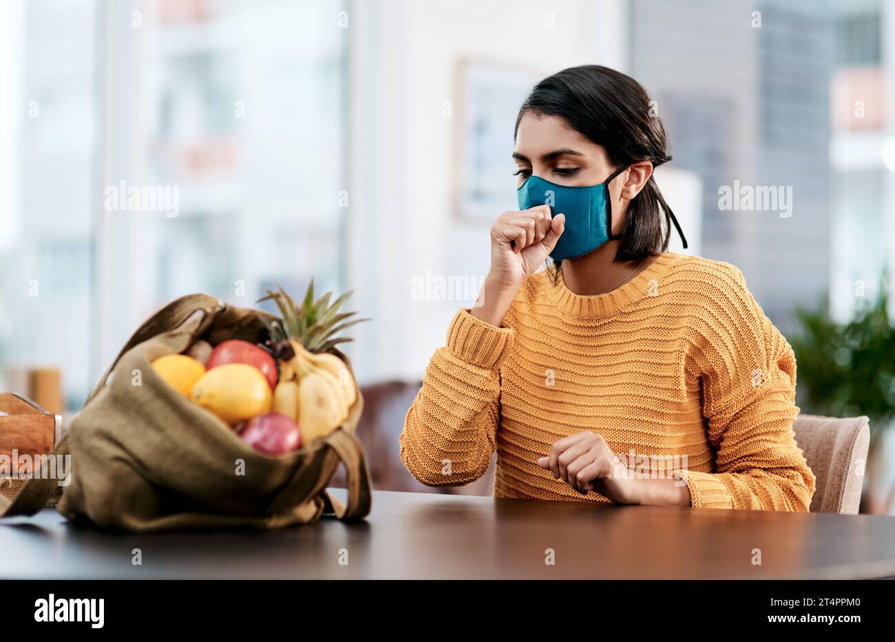 Non solo generi alimentari che potresti portare indietro dal negozio. una giovane donna mascherata che tossisce dopo essere tornata a casa dall'acquisto di generi alimentari. Foto Stock