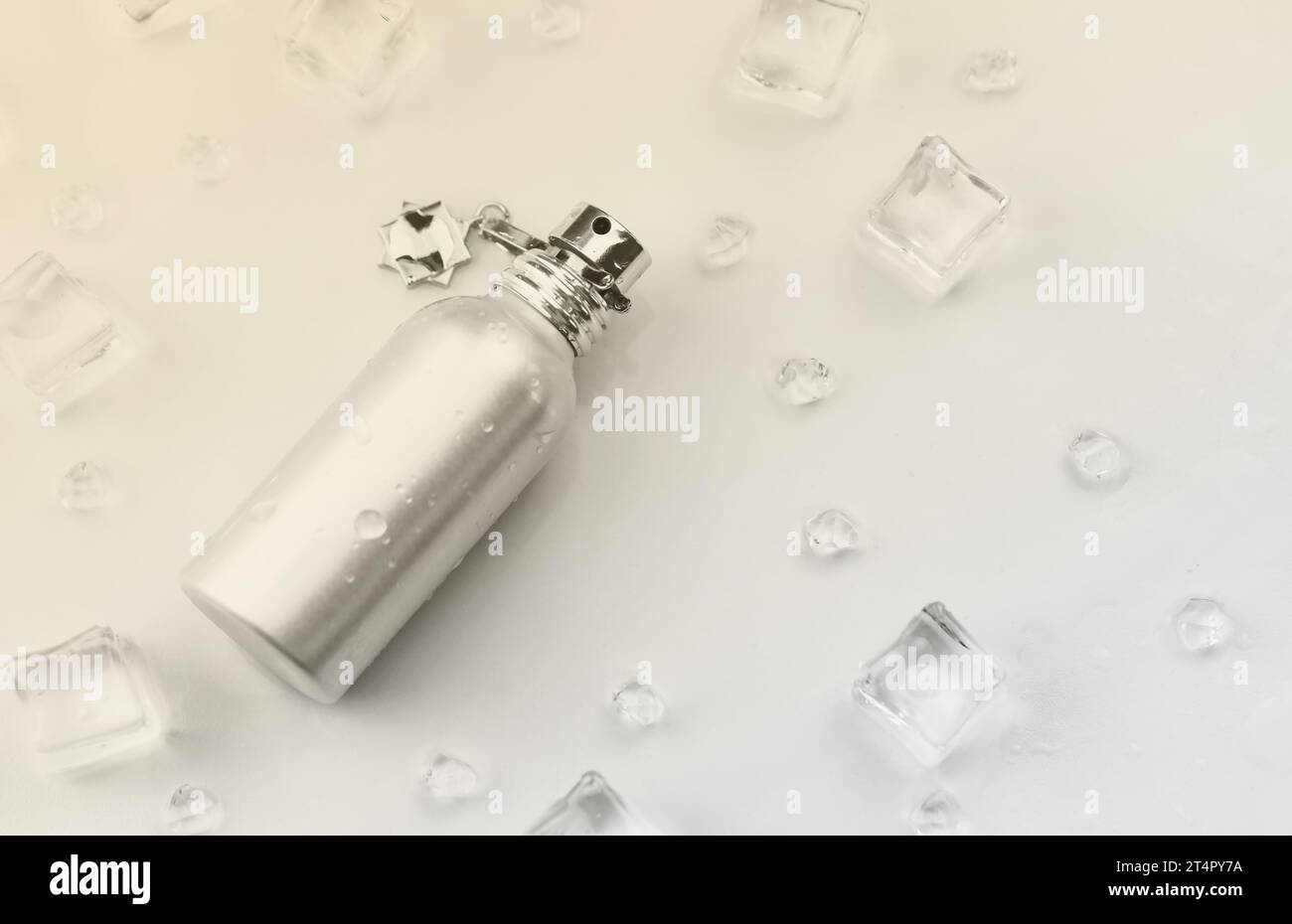 Bottiglia argentata di profumo femminile, fotografia oggettiva della bottiglia di profumo metallico in cubetti di ghiaccio e acqua su tavolo bianco. Vista dall'alto. Foto del prodotto mockup, concetto di freschezza e aroma Foto Stock