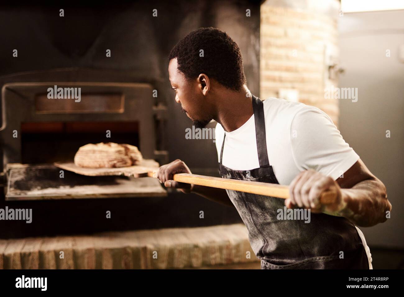 Supportare il proprio fornaio locale. un fornaio maschio che rimuove dal forno il pane appena sfornato. Foto Stock