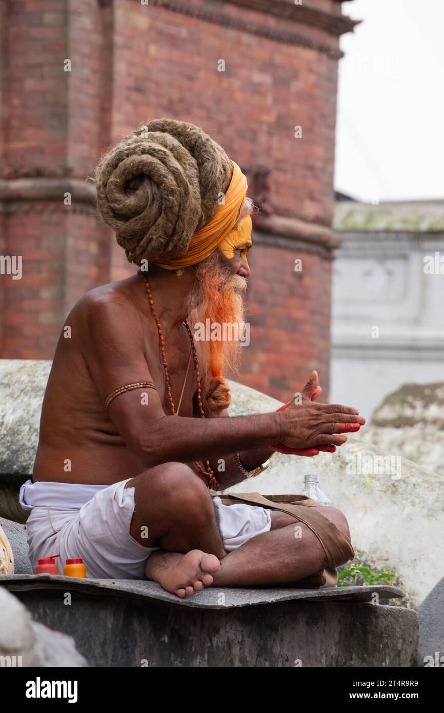 Kathmandu, Nepal: Le gambe hanno attraversato il guru indù in attesa che una famiglia prepari regali per i morti al tempio Pashupatinath, tempio indù dedicato a Shiva Foto Stock