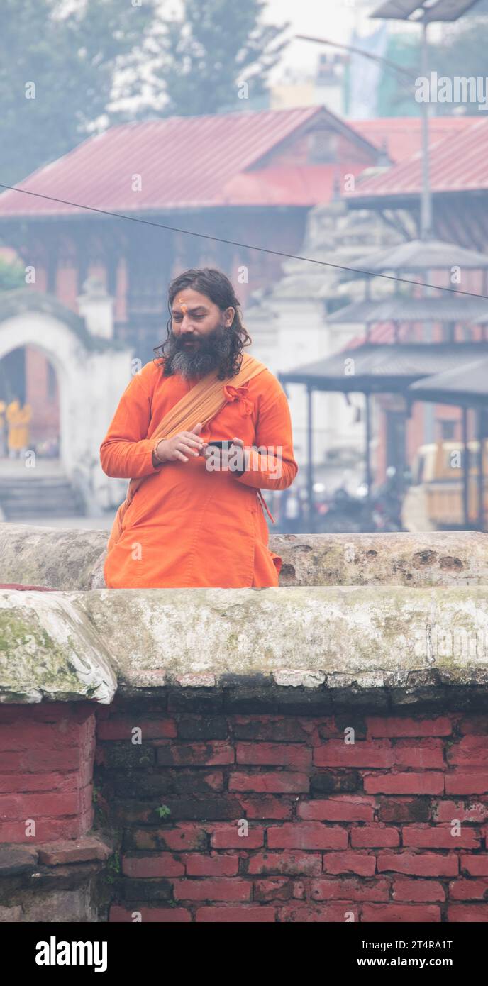Kathmandu, Nepal: Guru indù in attesa che una famiglia prepari regali per i morti al tempio Pashupatinath, famoso tempio indù dedicato a Shiva Foto Stock