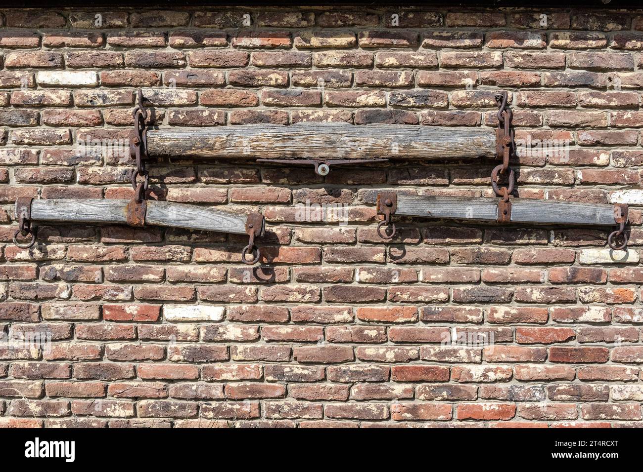 Vecchia imbracatura in legno o seesaw sul muro in mattoni del cortile della fattoria come decorazione, parti di un vecchio aratro trainato da cavalli, illuminato dalla luce del sole nelle giornate di sole Foto Stock