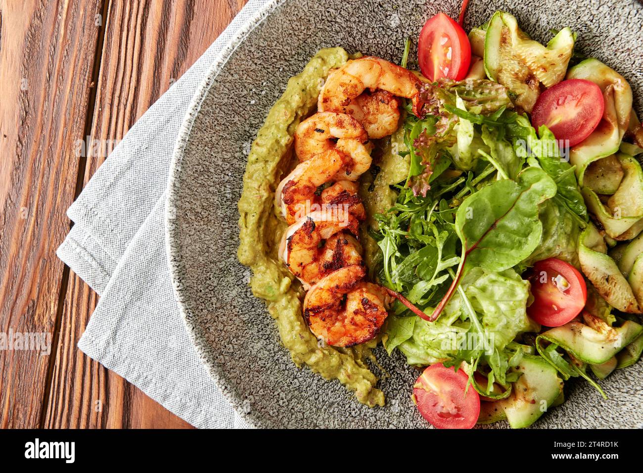 Gamberetti grigliati serviti con pesto, mix di insalate, zucchine grigliate e pomodori ciliegini freschi in un recipiente grigio. Foto Stock