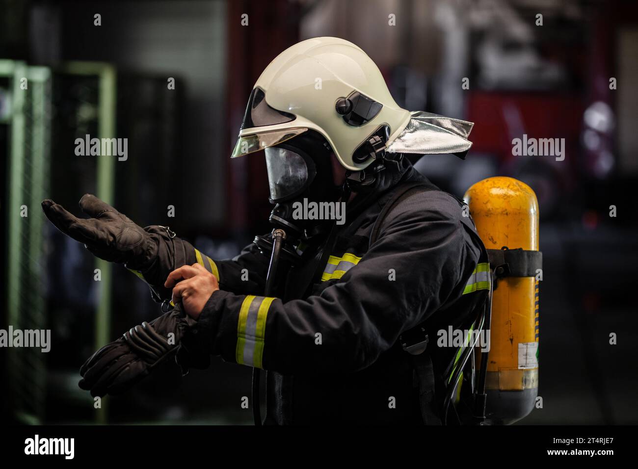 ritratto del pompiere con equipaggiamento completo e maschera di ossigeno. Indossare guanti protettivi . autocarri antincendio sullo sfondo. Foto Stock