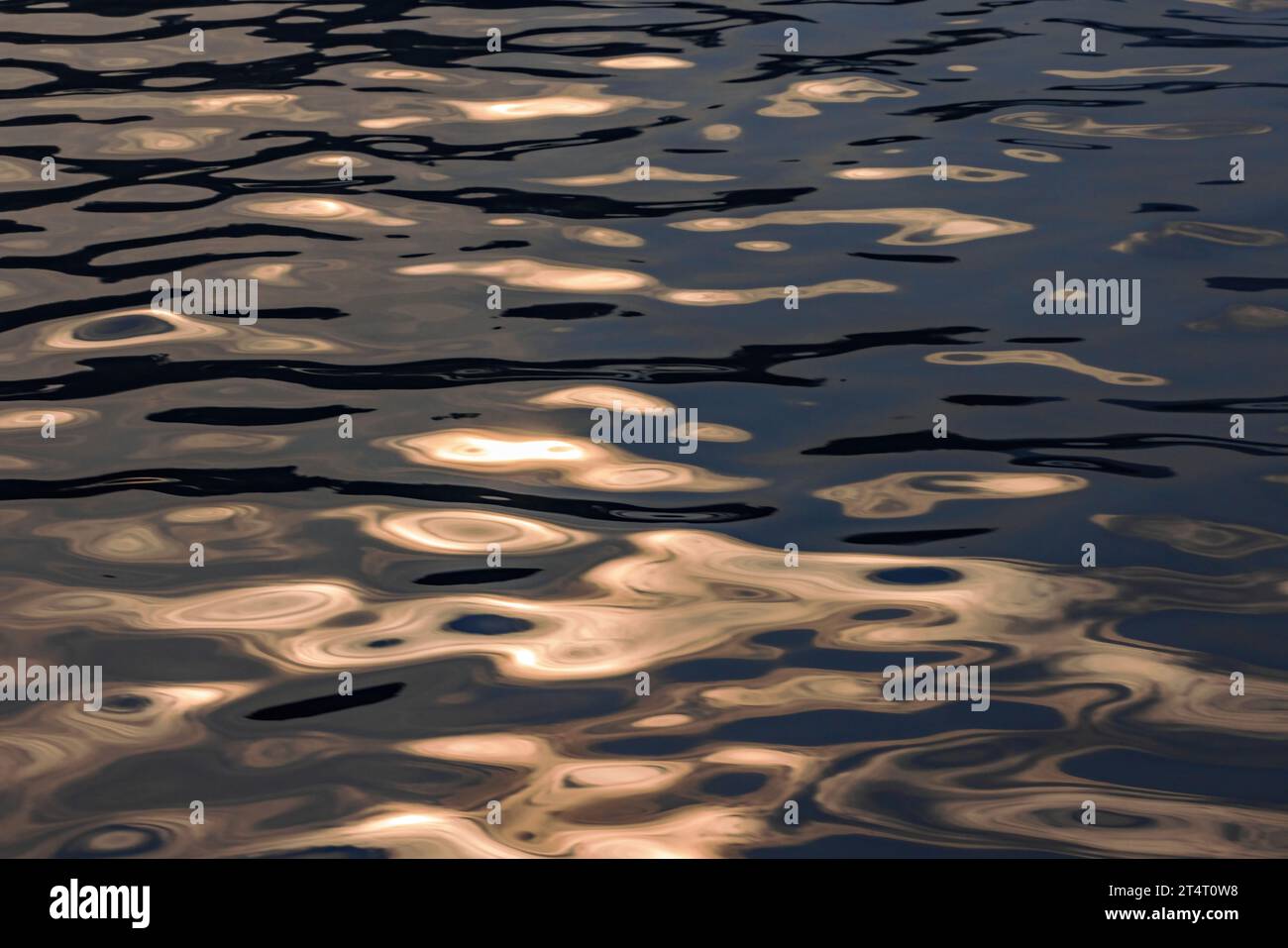 Ondulazioni d'acqua e onde riflettono il sole estivo reso nebbioso e scuro dal fumo di fuoco selvatico sull'oceano a Vancouver, Canada. Motivi e forme arancioni. Foto Stock