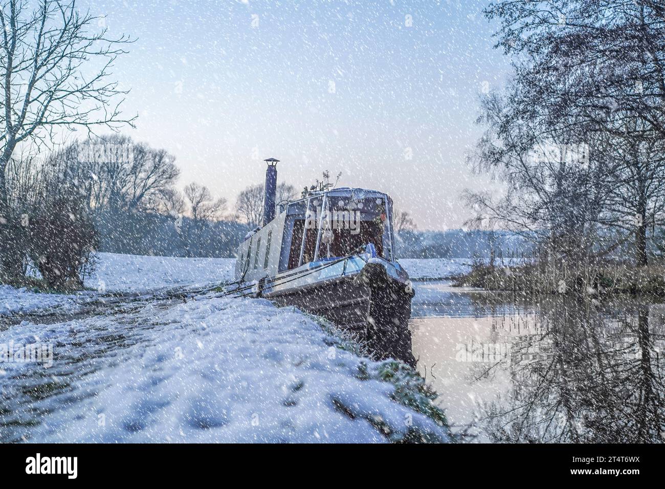 La barca stretta del Regno Unito ormeggiava su un canale del Worcestershire vicino a una sponda innevata e a un sentiero con neve a terra e neve che cade. Foto Stock