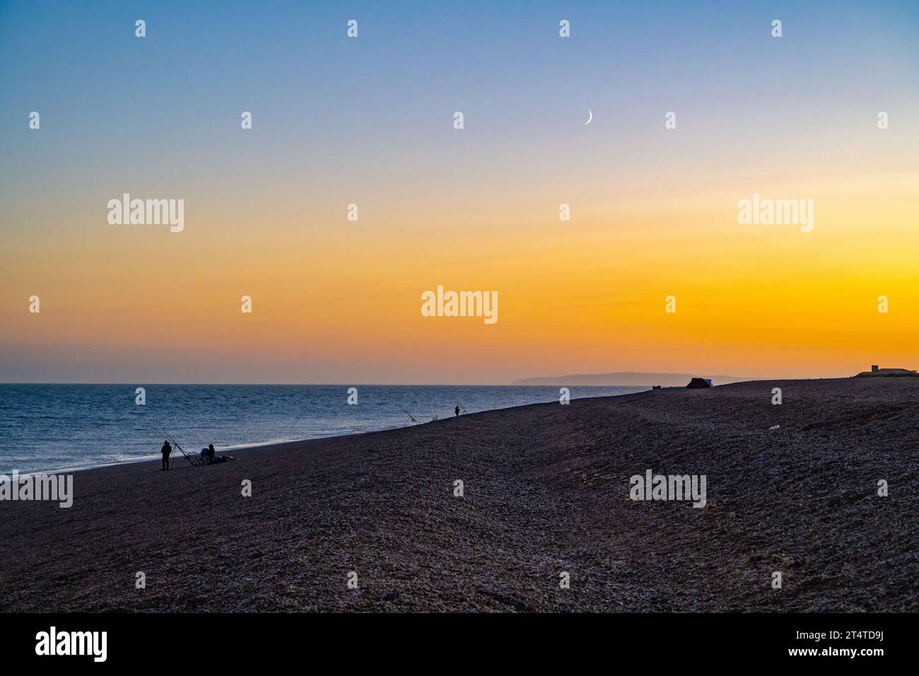 Fshermen che pesca sulla spiaggia di Dungeness, Kent, al tramonto Foto Stock