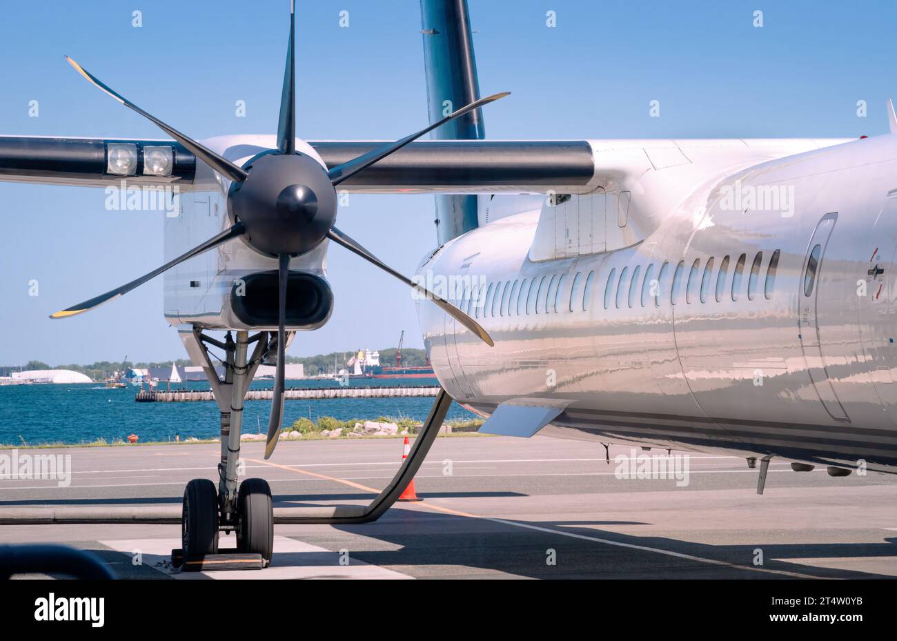 Primo piano dell'elica nera a sei pale e parte dell'ala e della fusoliera di moderno aereo di linea turboelica bianco nell'Aeroporto di Toronto City con tratto di blu Foto Stock