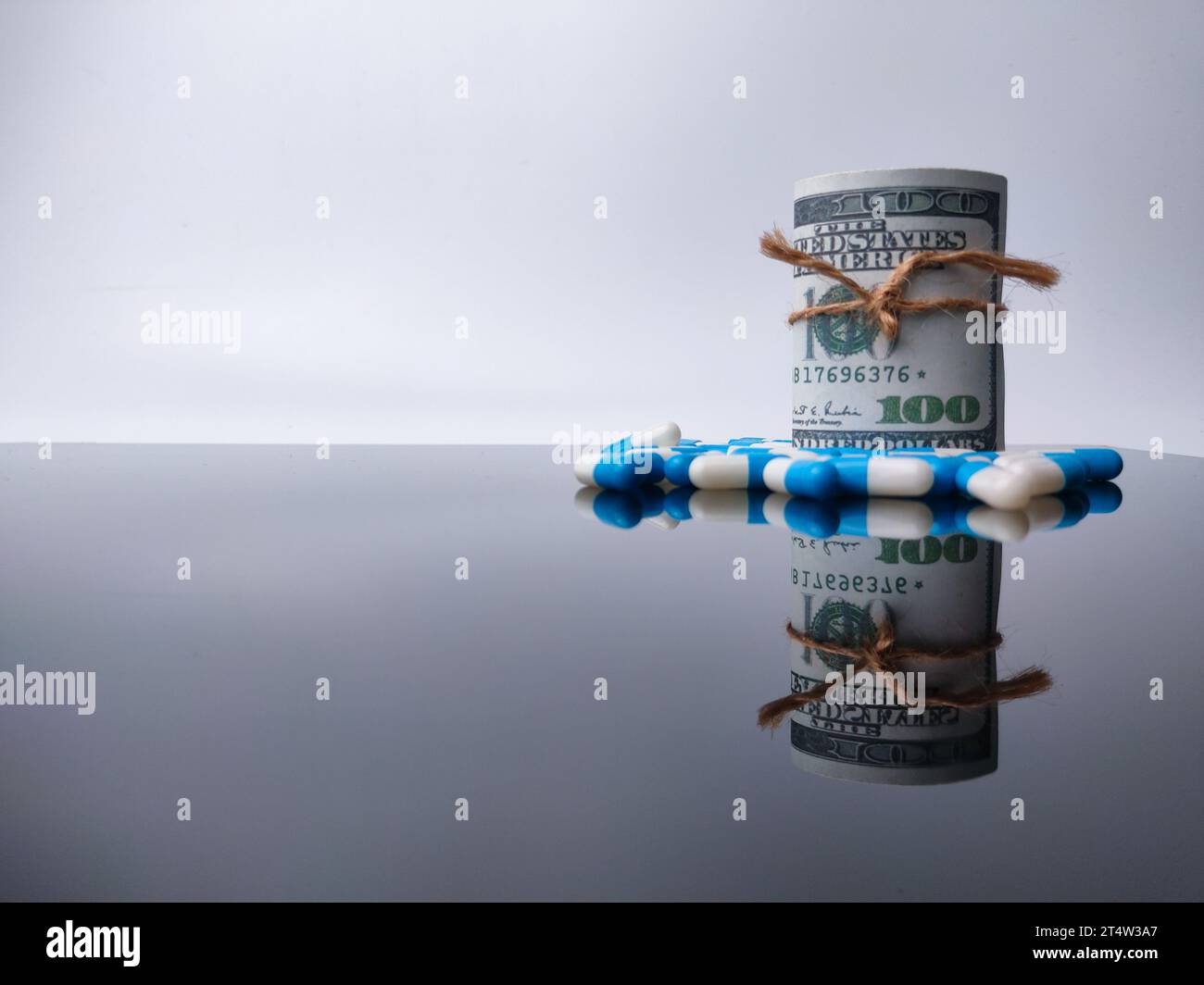 Banconote e medicine con riflesso su una tavola acrilica nera con spazio per la copia. Foto Stock