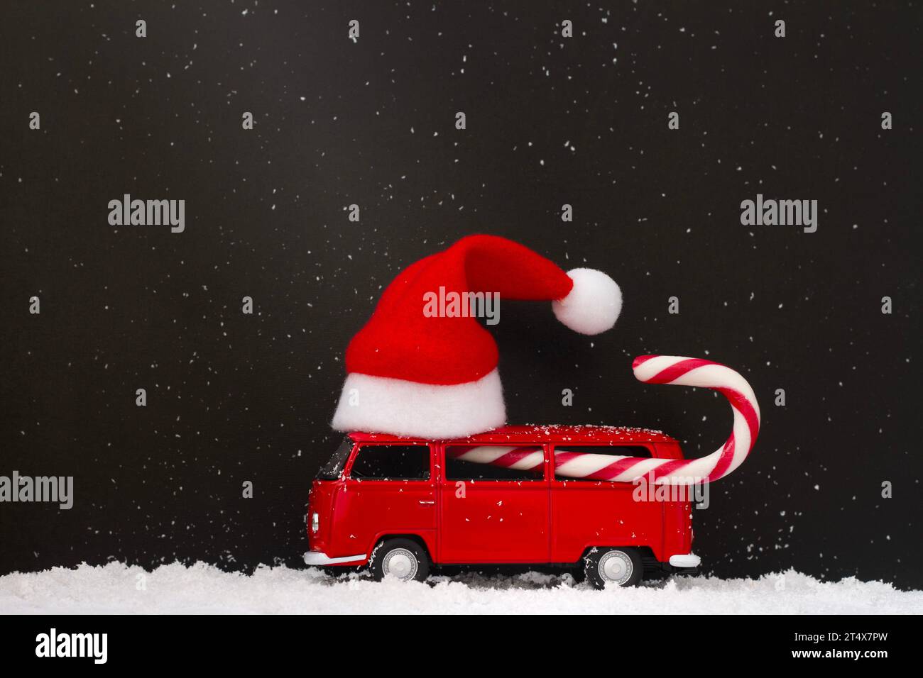 Macchinina giocattolo con cappello di Babbo Natale sul tetto e canna da zucchero nelle notti buie innevate. Sfondo creativo natalizio Foto Stock