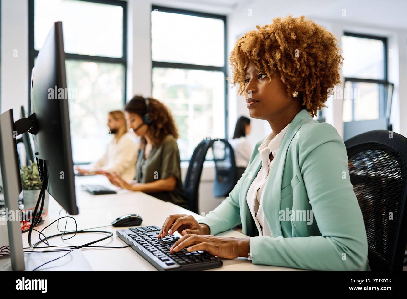 Donna africana che usa un computer seduto su una scrivania di coworking Foto Stock