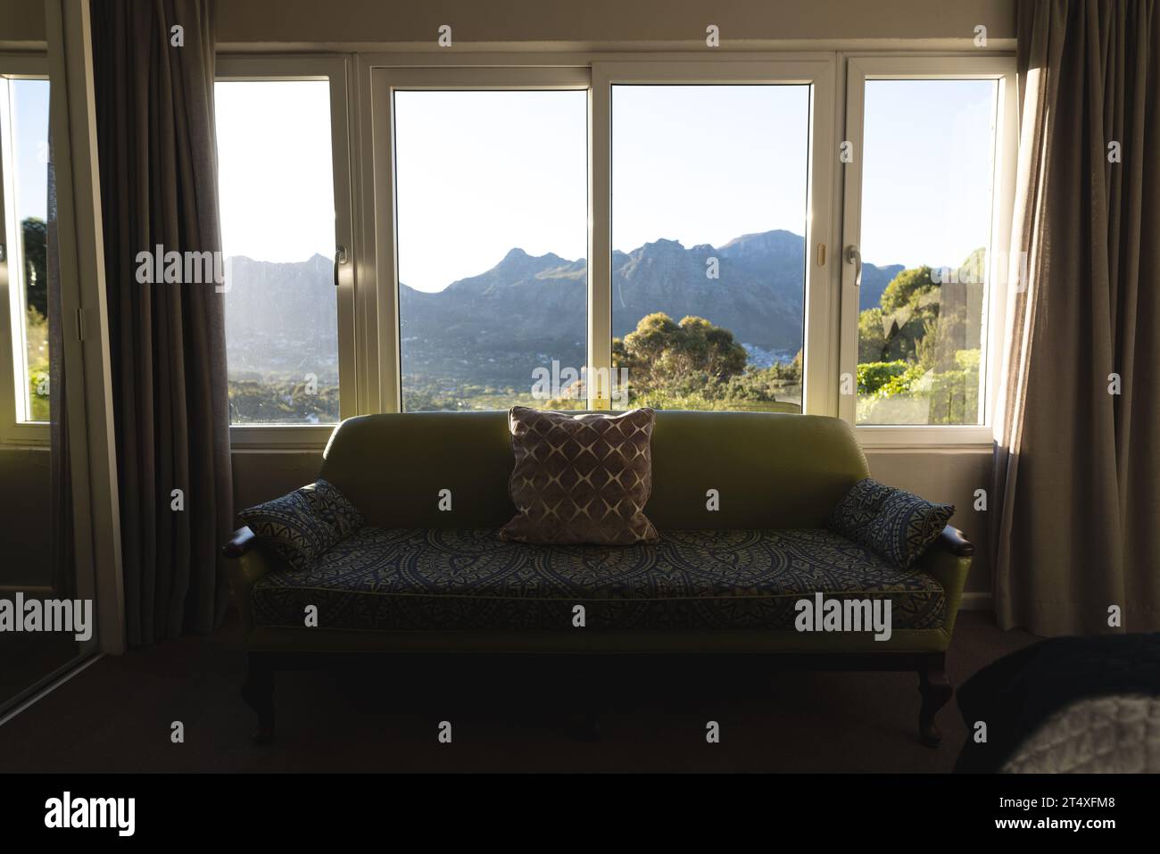 Interno del soleggiato soggiorno domestico con divano a finestra con vista sulle montagne, spazio fotocopie Foto Stock