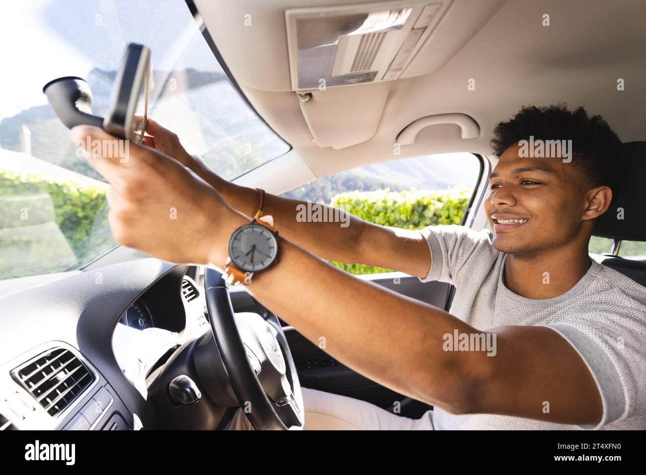 Felice uomo afro-americano che regola lo specchietto retrovisore in auto nelle giornate di sole Foto Stock