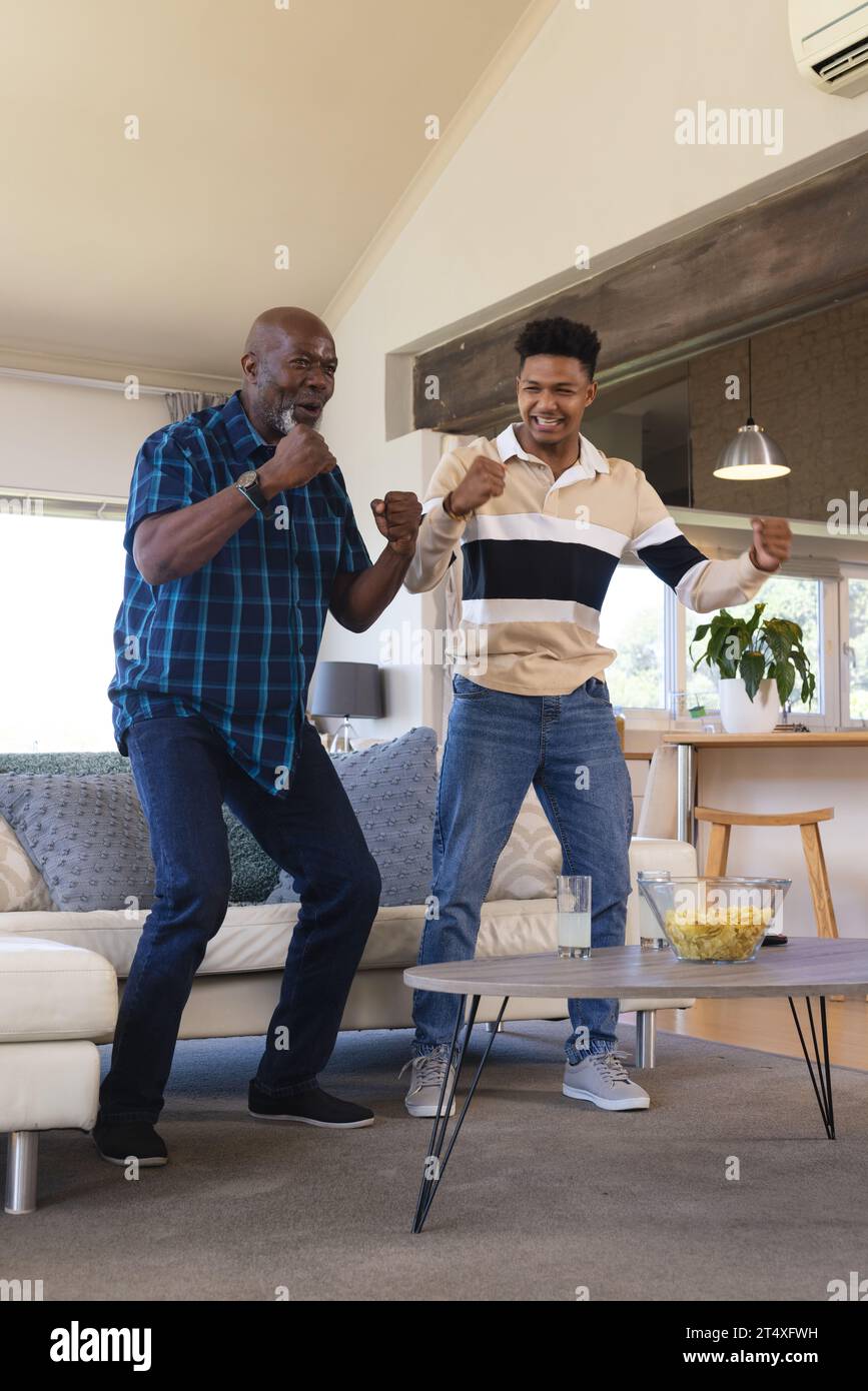 Eccitato padre afroamericano e figlio adulto in piedi celebrando la vittoria dello sport in tv, spazio copia Foto Stock