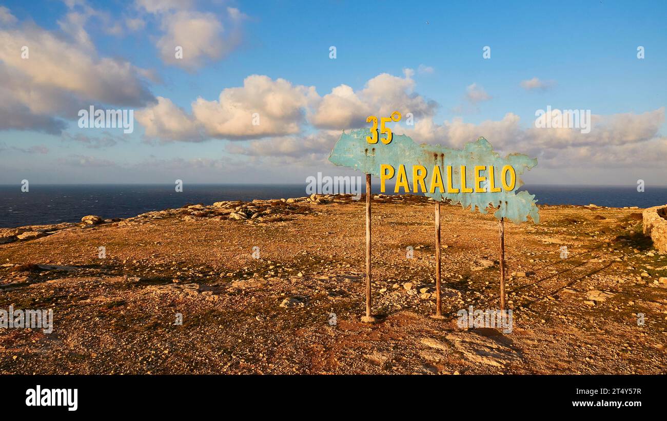 Cartello, più lontano, 35 parallelo, luce nel tardo pomeriggio, terreno roccioso, cielo nuvoloso azzurro, 35 latitudine, isola di Lampedusa, provincia di Agrigento, pelagica Foto Stock