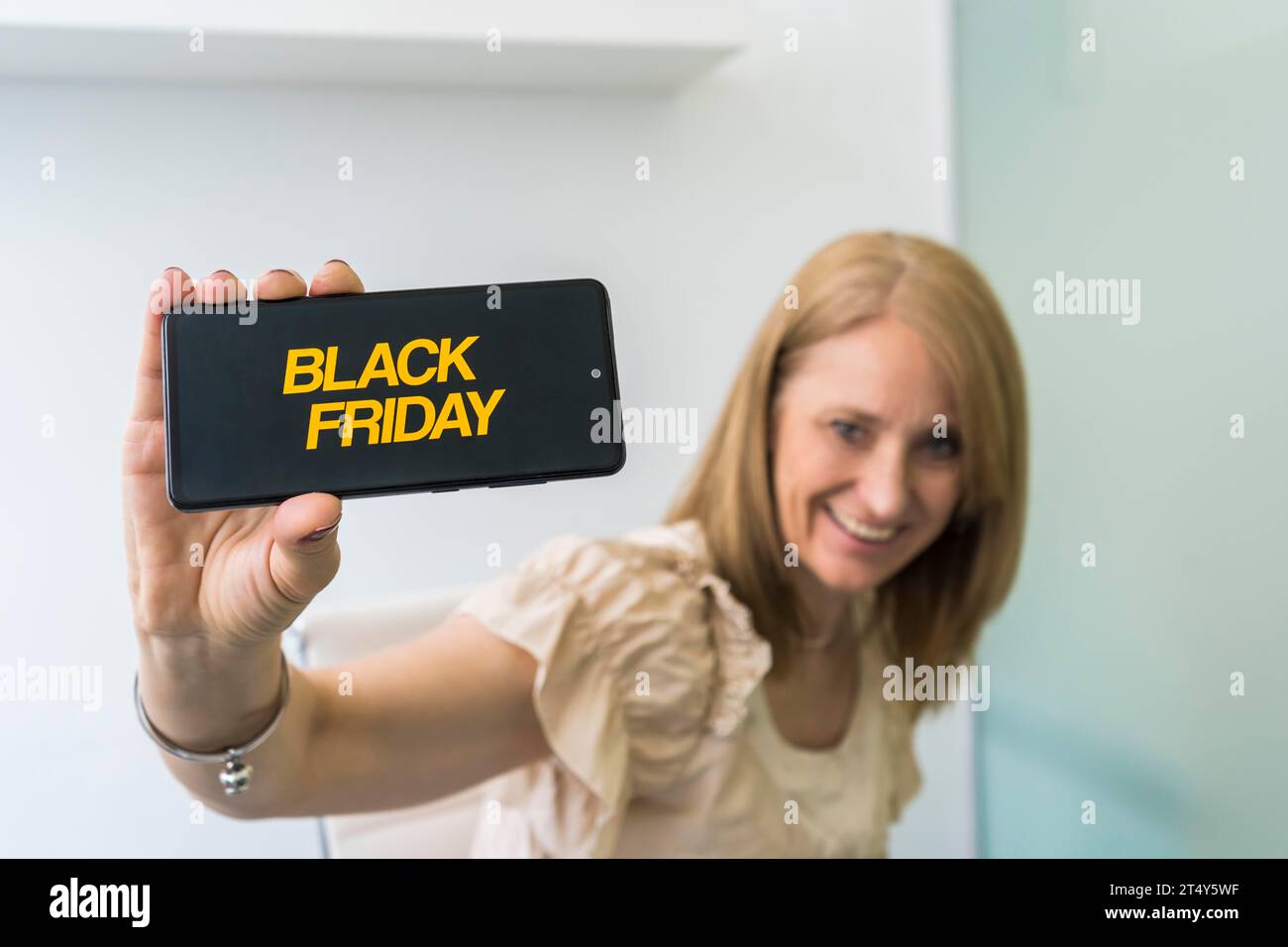 Bella donna di mezza età che mostra uno smartphone con la pubblicità del Black Friday sullo schermo Foto Stock