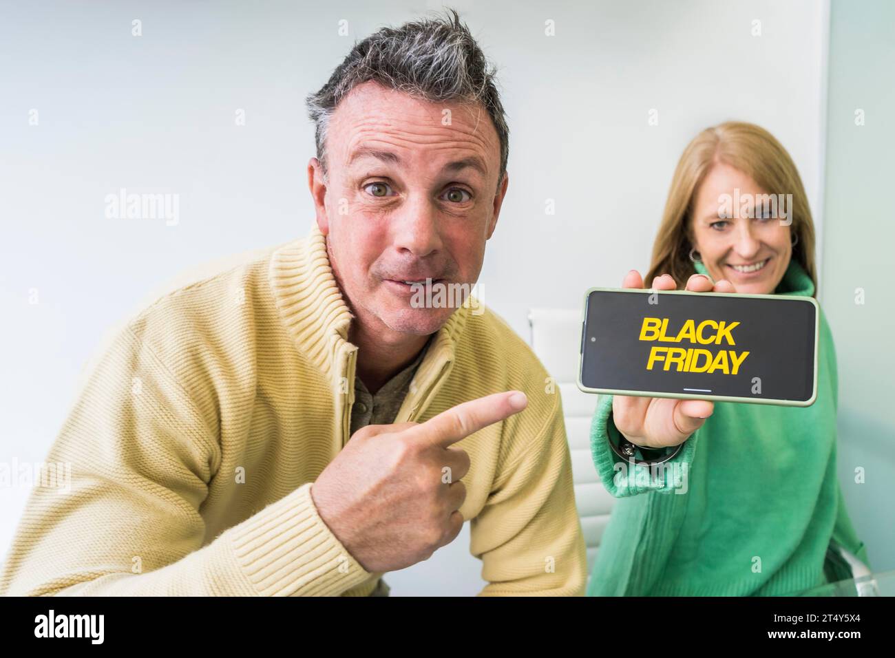 Un uomo mostra il suo smartphone con la pubblicità del Cyber Monday sullo schermo con sua moglie al suo fianco Foto Stock
