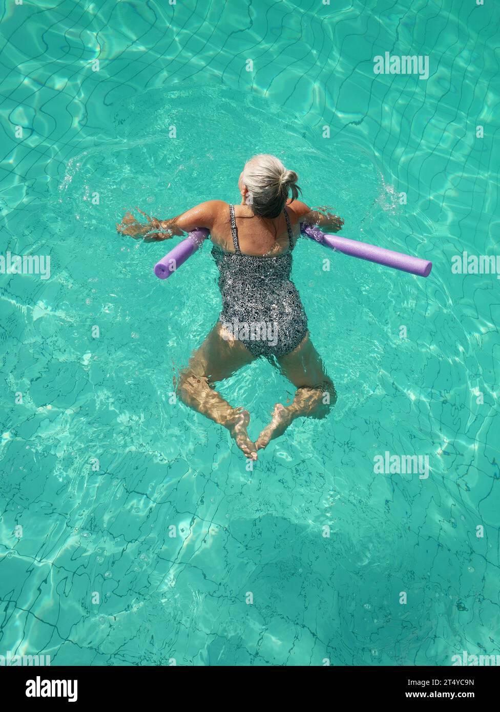 Vista dall'alto di una donna di 50 anni che nuota da sola in piscina in vacanza utilizzando un noodle bouyancy aid. Foto Stock