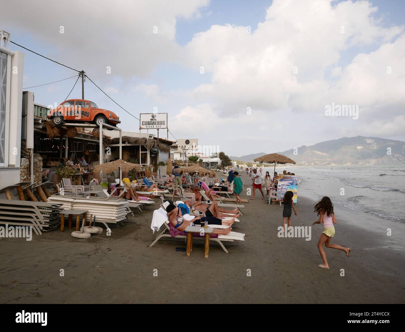 I turisti di fine stagione si riuniscono intorno a un ultimo bar sulla spiaggia aperto rimasto. Zante, Grecia. Foto Stock