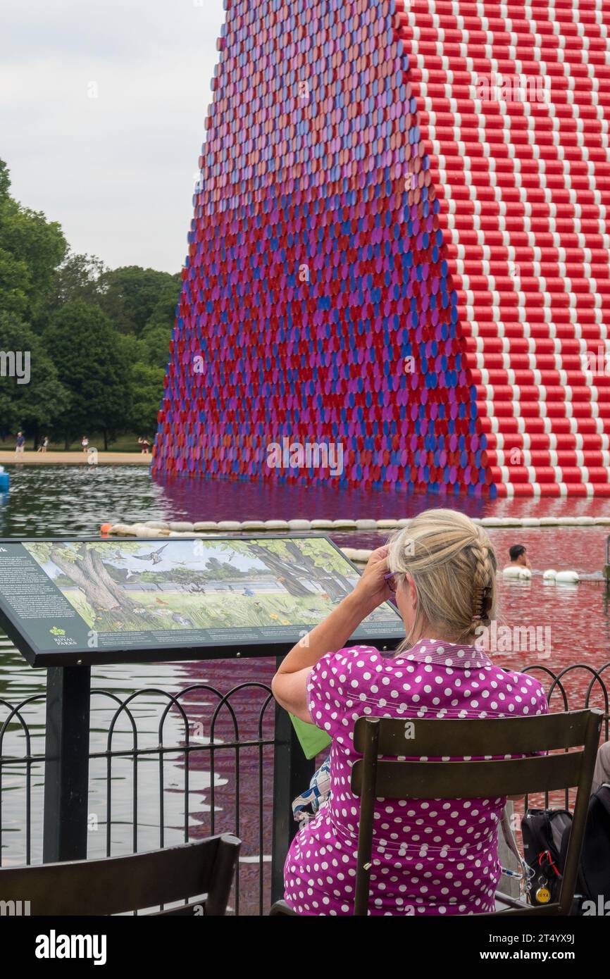 Donna il cui modello di abito è in perfetta armonia con la statua di Christo e Jeanne-Claude: La London Mastaba. Hide Park, Londra, Regno Unito. Foto Stock
