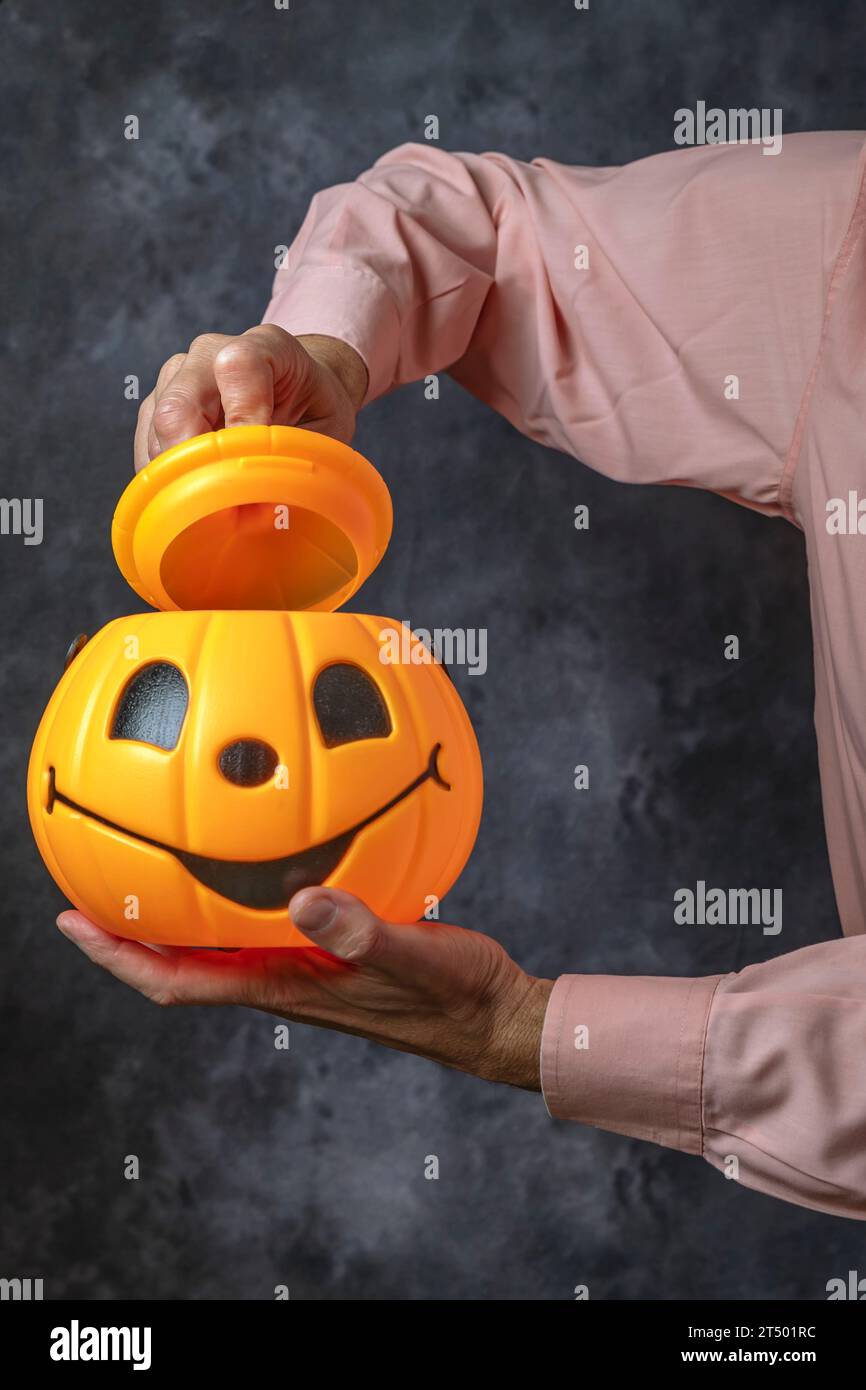 Un uomo con una camicia rosa apre il coperchio di un contenitore a forma di zucca di halloween Foto Stock