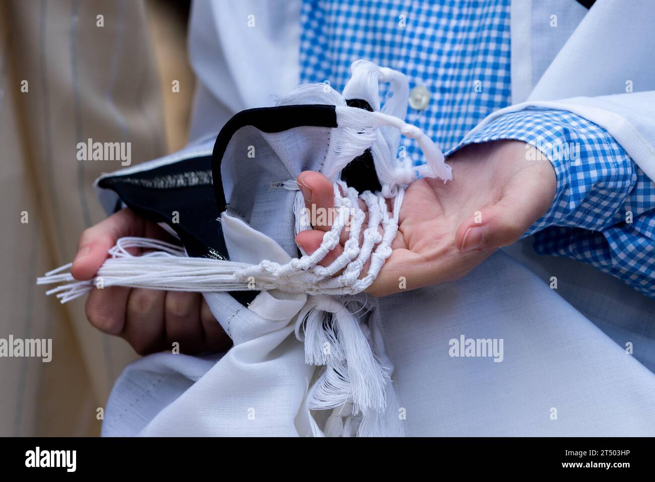 Un giovane ebreo tiene le corde del suo tallit o tzitzit mentre recita la preghiera Shema Yisrael durante un servizio di preghiera mattutino ortodosso. Foto Stock