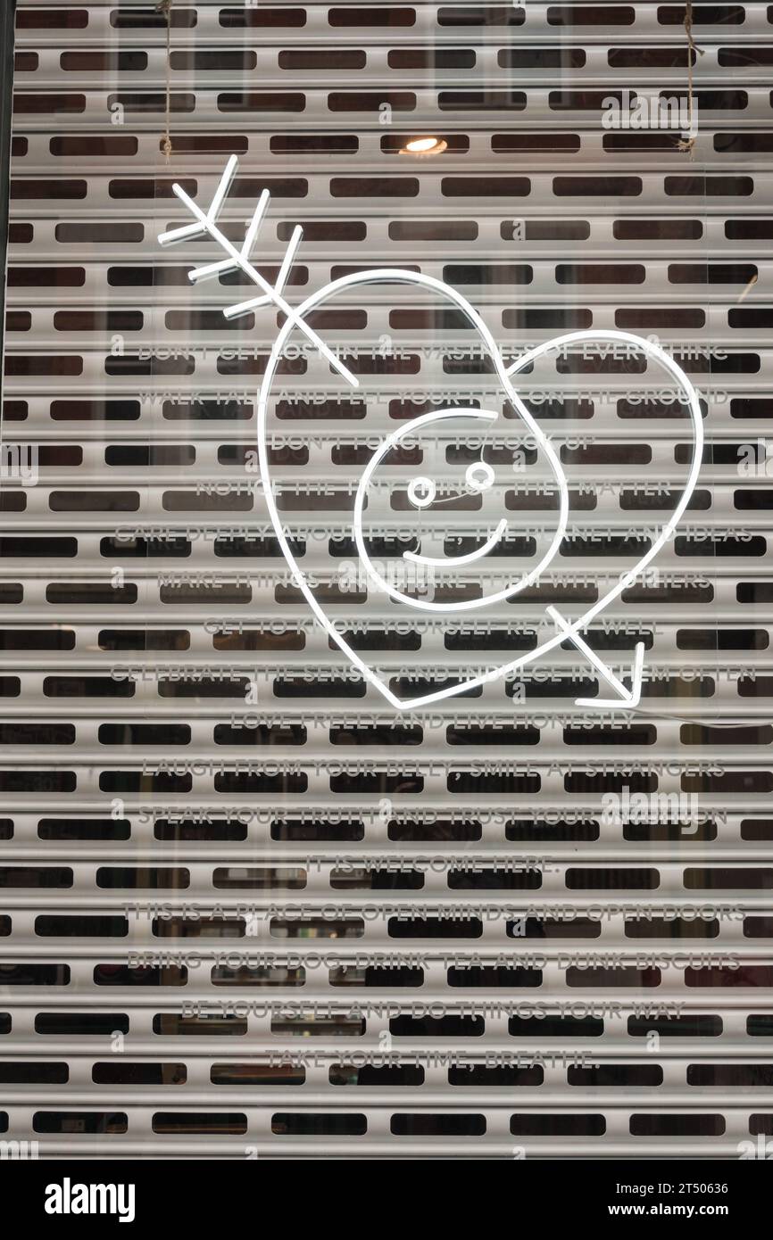 Un sorridente cuore amoroso trafitto dalla freccia di Cupido contro una griglia di sicurezza in metallo su una finestra di fronte al negozio Foto Stock