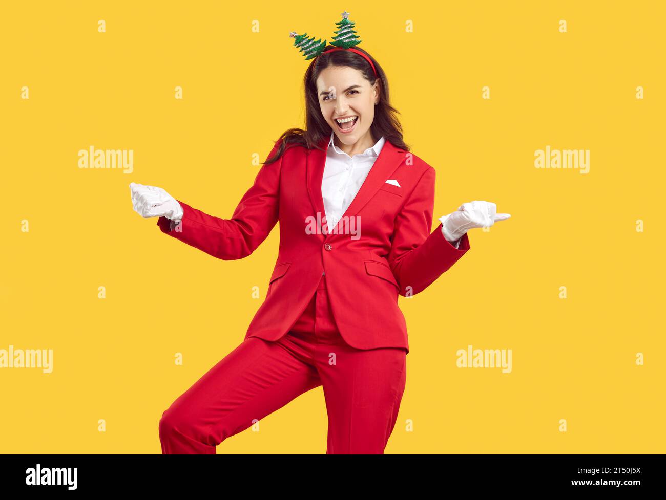 Bruna natalizia emozionante e danzante che indossa balli in stile Babbo Natale su sfondo giallo. Foto Stock