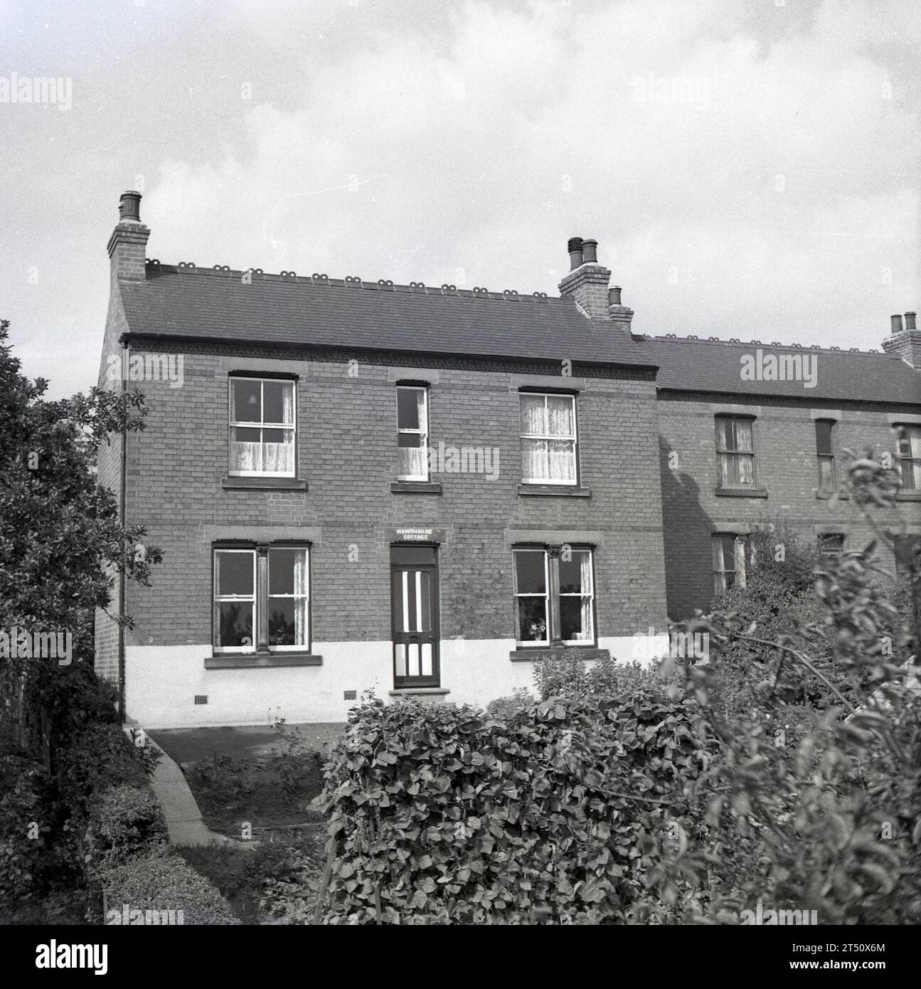 1950, storica, vista di una casa indipendente in mattoni vittoriani con facciata piatta, su un crinale, serra in giardino, Oldham, Inghilterra, REGNO UNITO. Nome sulla porta, Hawthorne Cottage. Foto Stock
