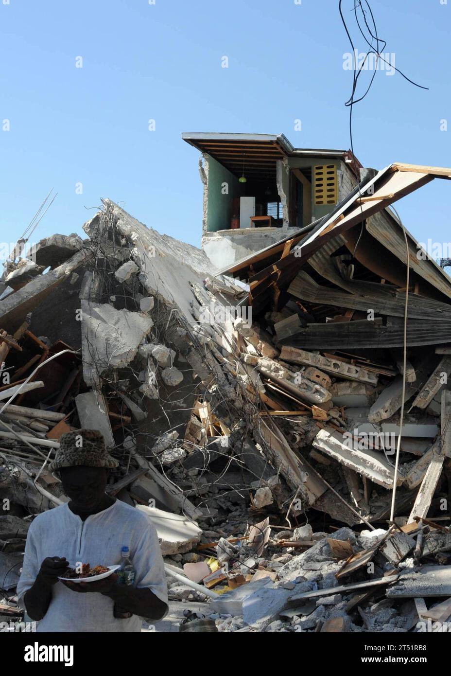 1001216410J-242 PORT-AU-PRINCE, Haiti (21 gennaio 2010) Un uomo haitiano mangia un pasto davanti a un edificio distrutto durante il terremoto di magnitudo 7,0 nella nazione caraibica di Haiti il 12 gennaio 2010. Le unità militari statunitensi e internazionali e le agenzie umanitarie civili stanno conducendo operazioni umanitarie e di soccorso in caso di calamità nell'ambito dell'operazione Unified Response in seguito al terremoto. Marina Foto Stock