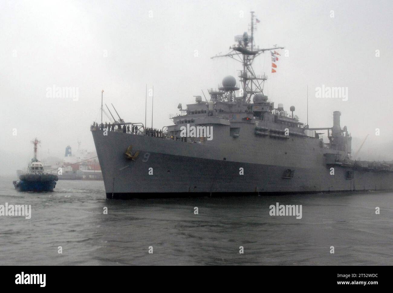 0906100807W-157 SASEBO, Giappone (10 giugno 2009) i marinai indossano le rotaie sotto pioggia battente a bordo della nave da trasporto anfibia USS Denver (LPD 9) mentre i rimorchiatori la guidano dal suo ormeggio per partecipare all'esercizio Talisman Saber 09. Il talismano Saber è un'esercitazione combinata australiana e statunitense progettata per preparare entrambe le nazioni nella pianificazione delle azioni di crisi e nell'esecuzione delle operazioni di emergenza. Foto Stock