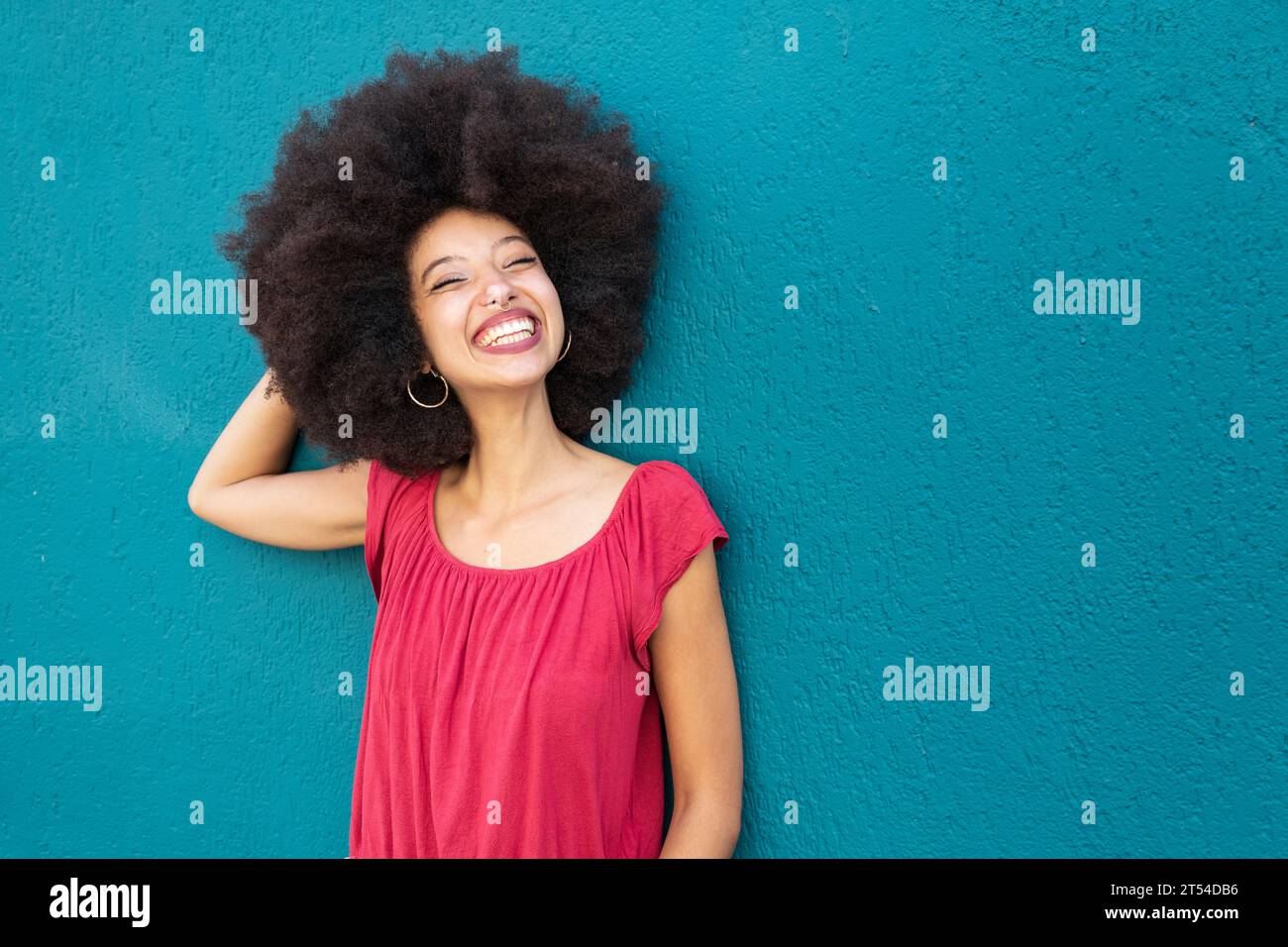 Ritratto di una donna marocchina sorridente in abiti casual con acconciatura afro in piedi contro una parete blu brillante Foto Stock