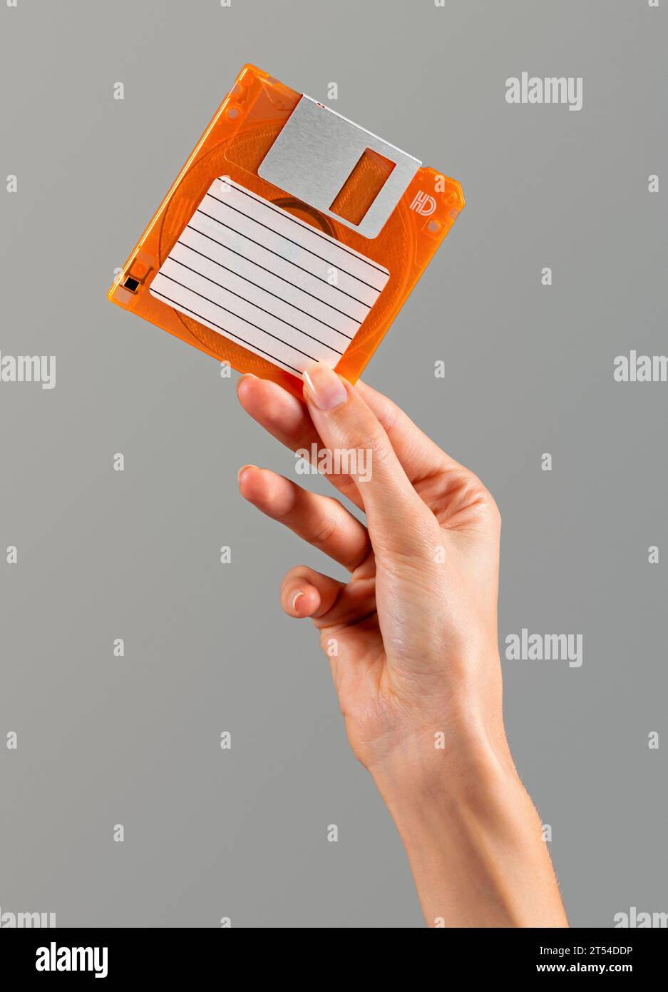 Donna anonima con dita ben curate che mostra un floppy disk di colore arancio retrò con carta per etichette vuota e telaio metallico scorrevole sulla parte superiore in luce Foto Stock