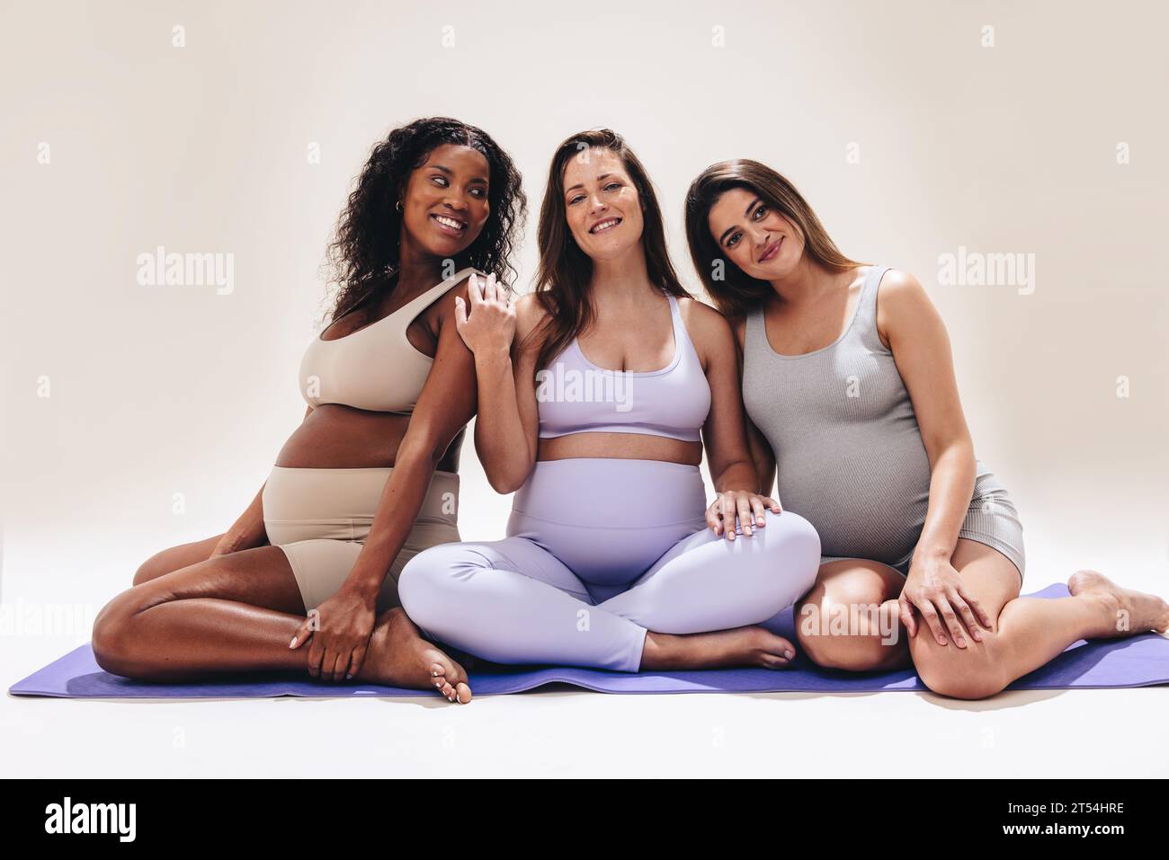 Le madri in attesa praticano lo yoga prenatale in uno studio. Sorridenti e felici, queste diverse donne danno priorità alla cura di sé, al benessere e alla forma fisica. Insieme, t Foto Stock