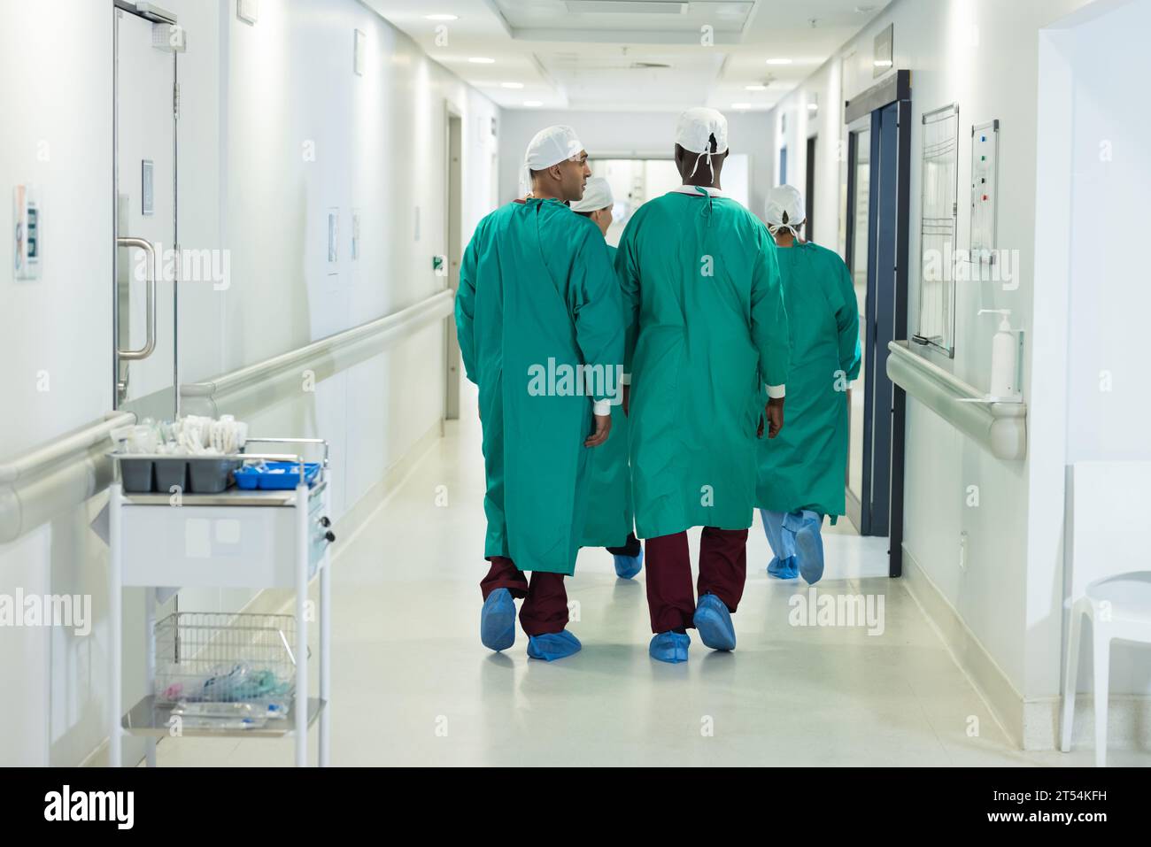 Diversi chirurghi maschili e femminili che indossano abiti chirurgici che camminano nel corridoio dell'ospedale Foto Stock