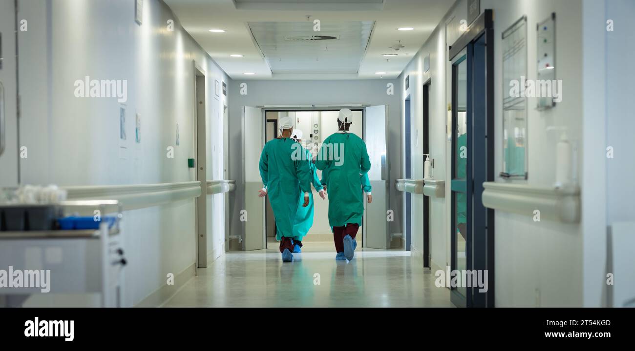 Diversi chirurghi maschili e femminili che indossano abiti chirurgici che camminano nel corridoio dell'ospedale Foto Stock