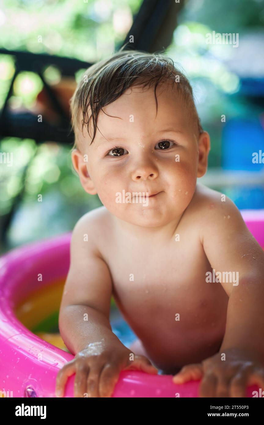 Un piccolo e carino bambino gioca con i giocattoli mentre fa il bagno in una piccola piscina colorata. Ora legale. Concetto di gioia e felicità. Amore e famiglia em Foto Stock