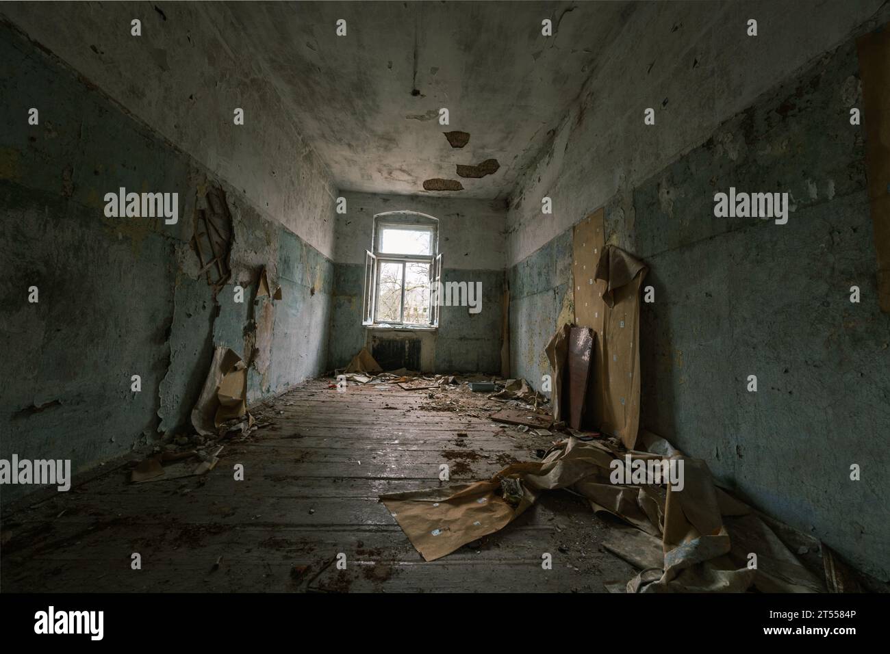 L'interno della camera abbandonata con pareti dipinte che si staccavano danneggiava la spazzatura dei mobili di legno sul pavimento sporco con soffitto sgretolato che mostrava aste di ferro Foto Stock