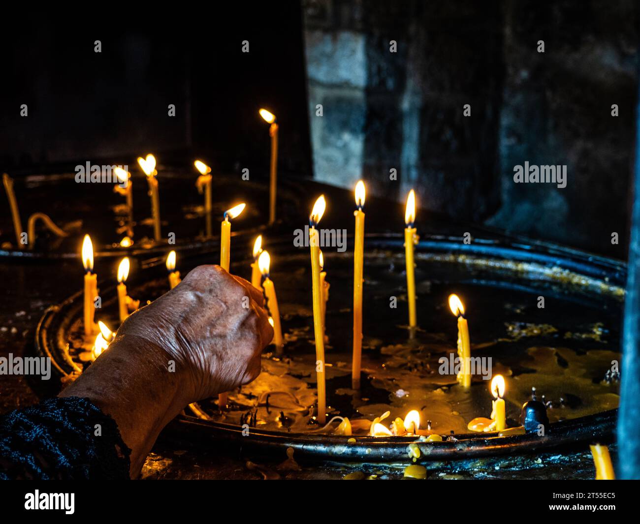 la mano della donna anziana che illumina una candela in chiesa Foto Stock