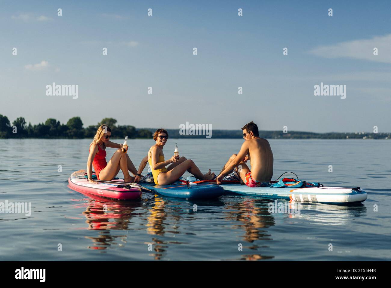 Amici che bevono birra durante le vacanze estive sul lago, paddleboard. Foto Stock