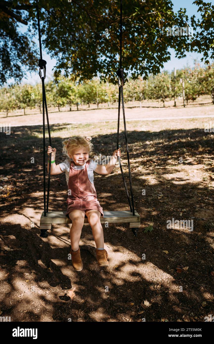 Bambino che oscilla sotto gli alberi alla fattoria Foto Stock