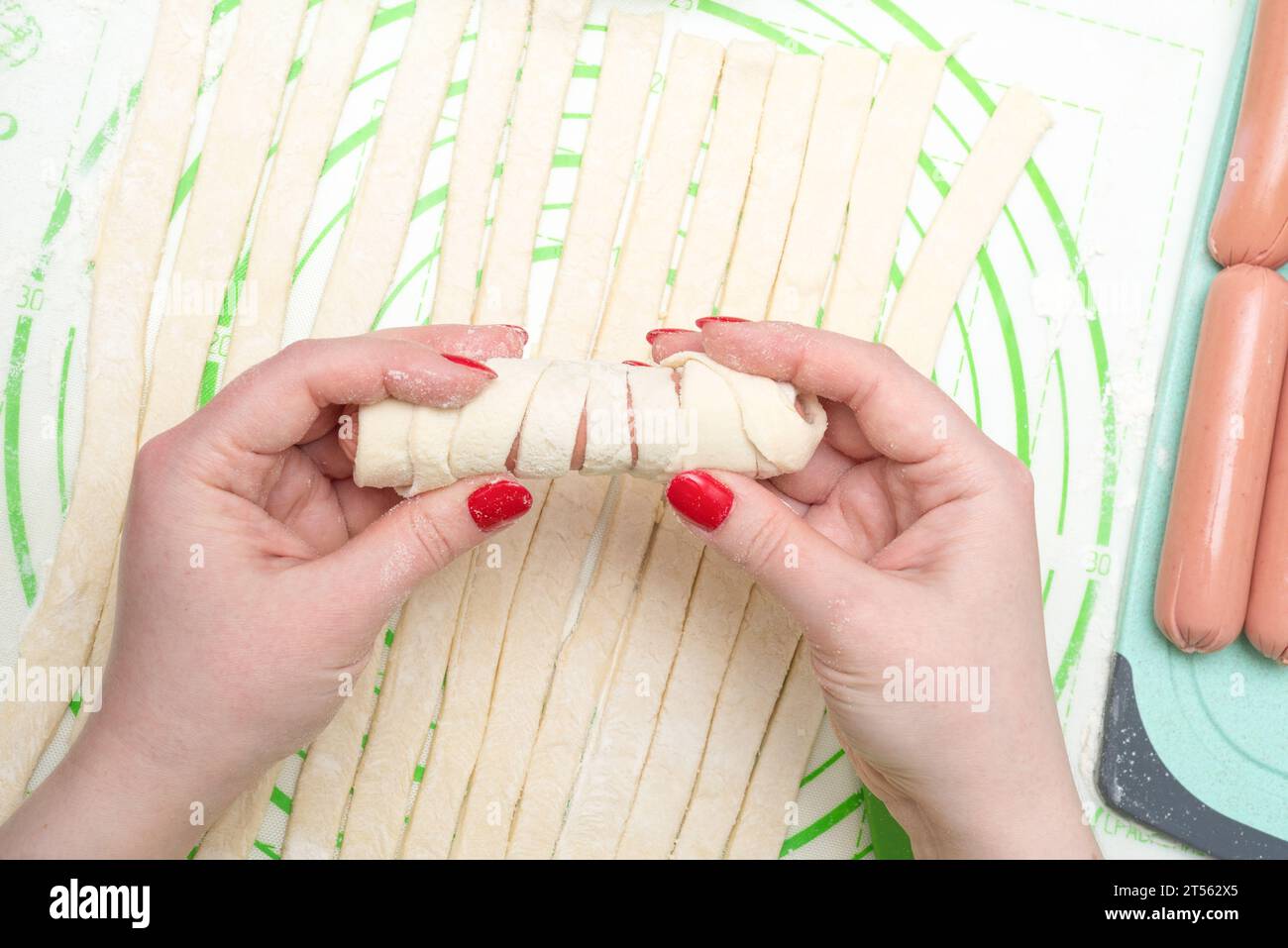 Salsiccia in impasto crudo nelle mani di una giovane donna con manicure. Il processo di preparazione delle salsicce nell'impasto. Foto Stock