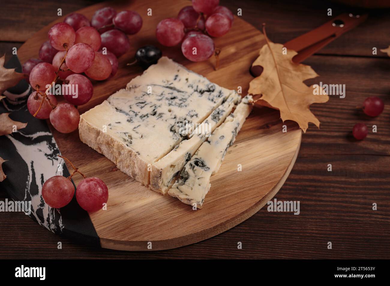 Piatto di formaggi servito con frutta autunnale e foglie secche Foto Stock