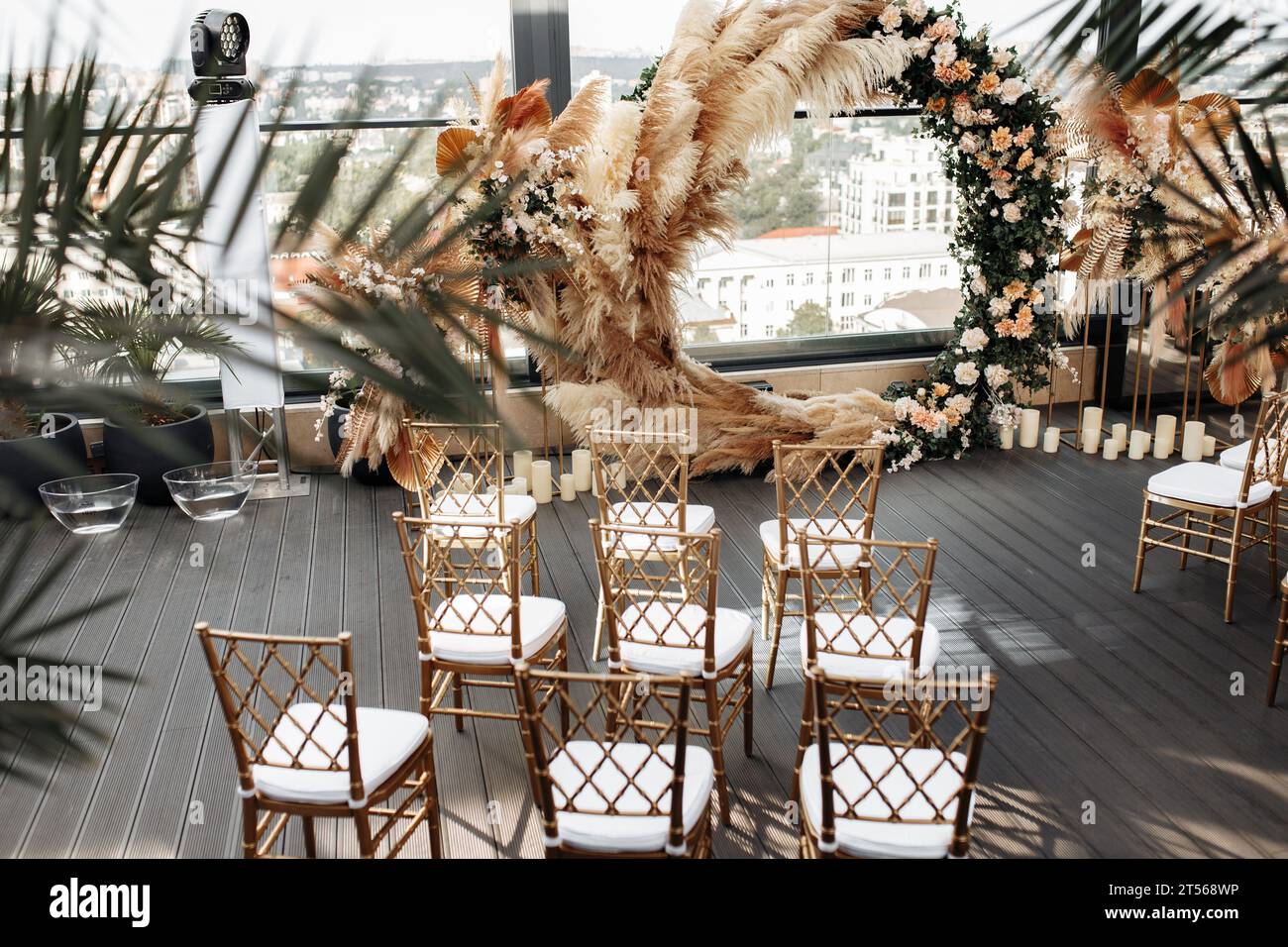 Vista laterale della terrazza decorata, arco di fiori e sedie stilizzate in lussuose tonalità oro. Arredamento moderno. Foto Stock