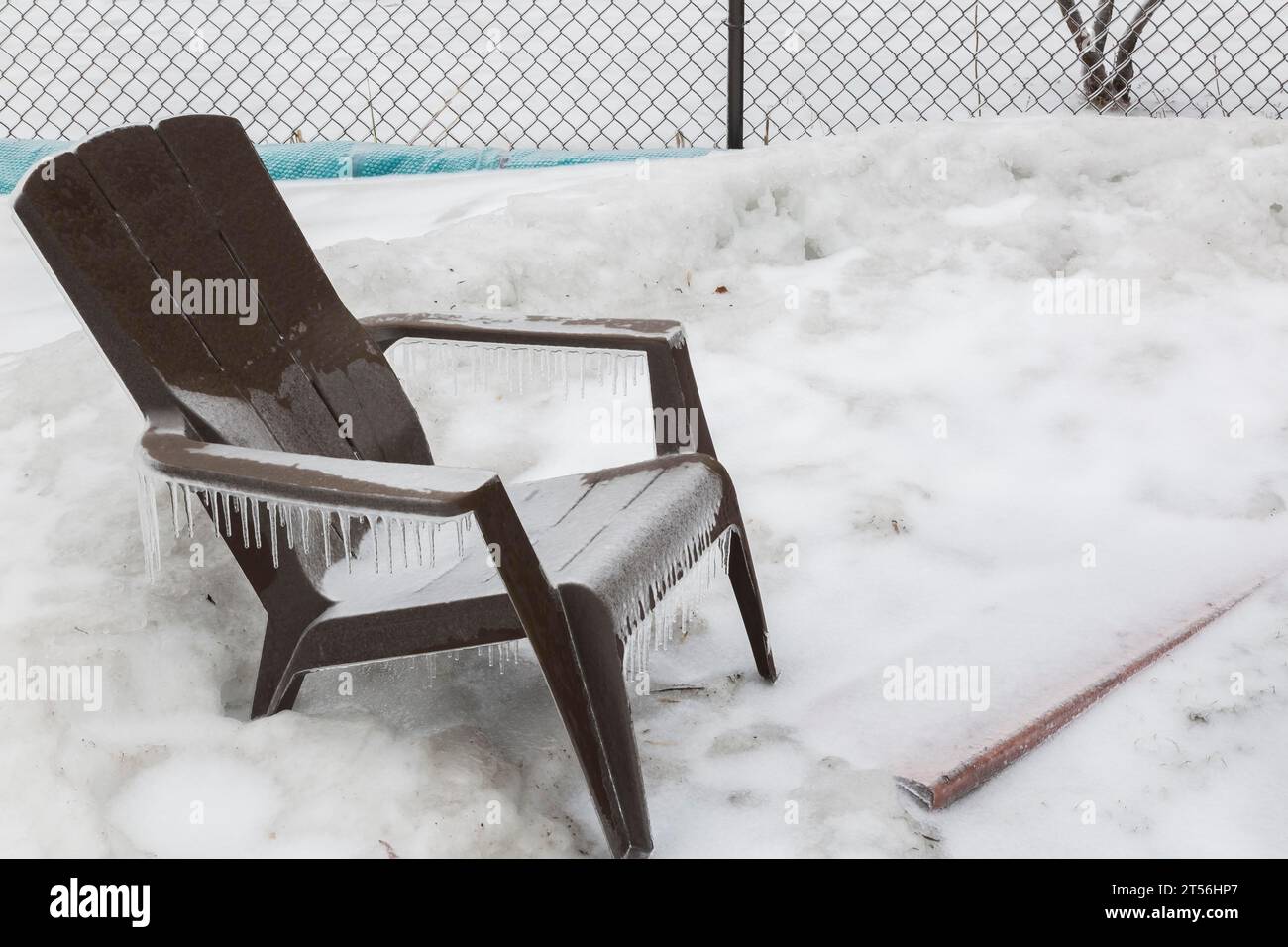 Poltrona Adirondack in plastica marrone coperta di ghiaccio nel cortile di casa dopo una pioggia ghiacciata all'inizio della primavera, Quebec, Canada Foto Stock