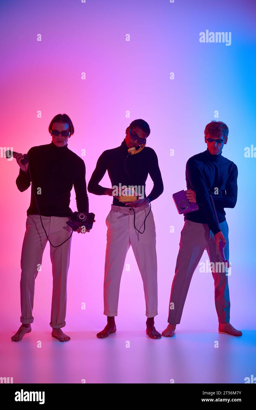 modelli maschili multietnici di bell'aspetto circondati da luci al neon in posa con telefoni fissi, uomini power Foto Stock