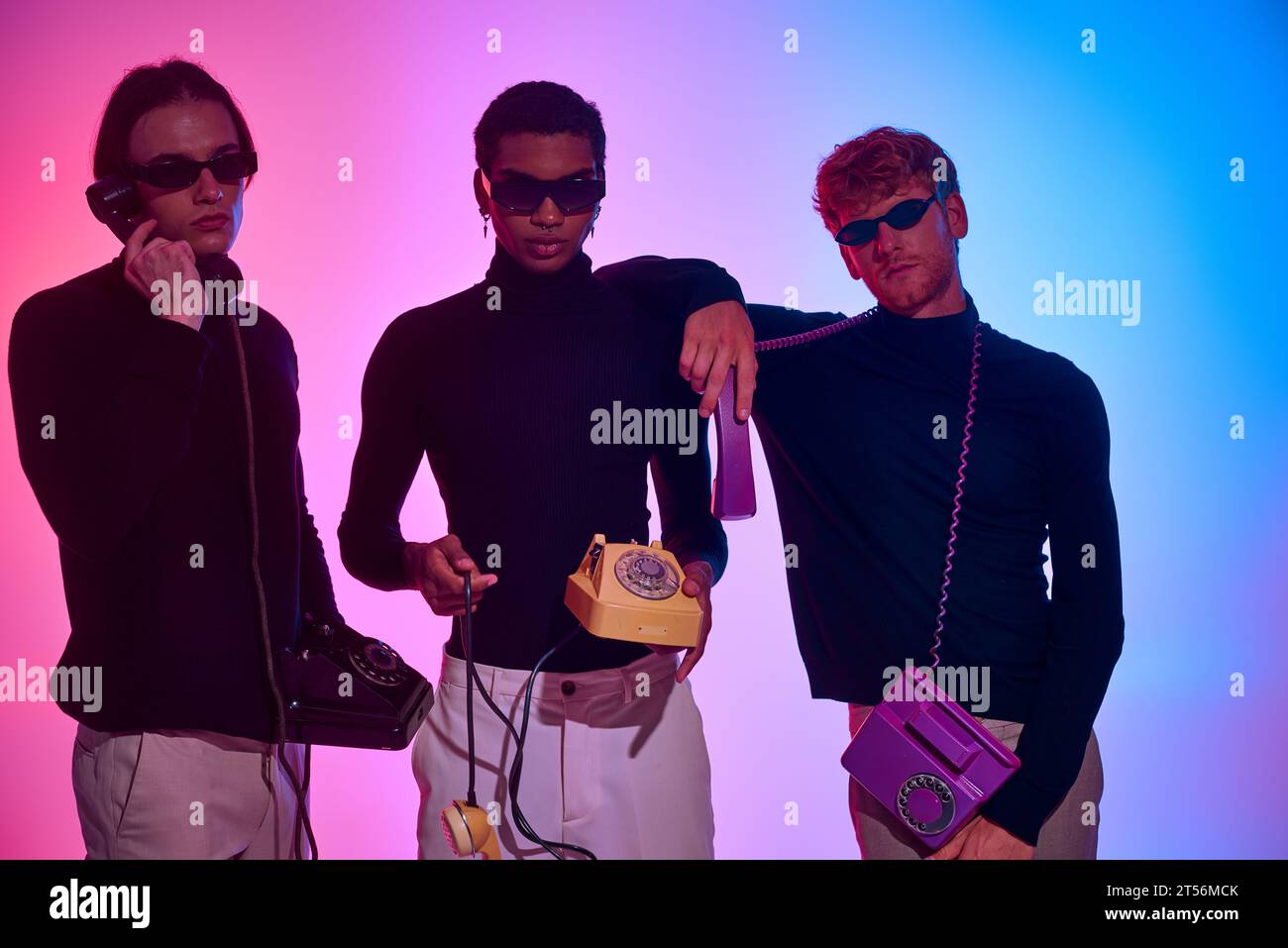 tre giovani uomini in abiti neri con telefoni fissi indossano occhiali da sole, concetto di moda Foto Stock