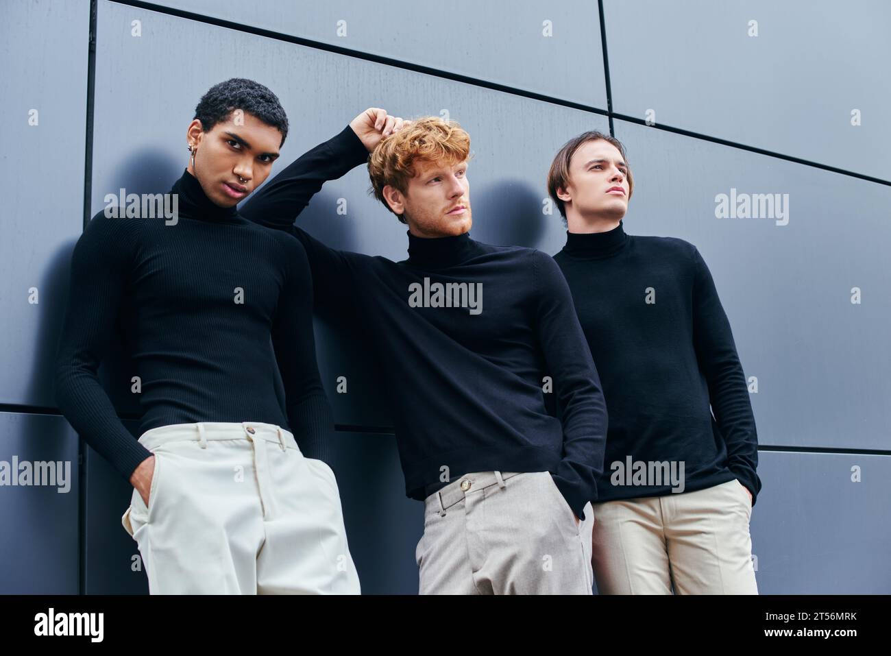 uomo dai capelli rossi che posa con la mano dietro la testa tra gli altri uomini a muro, scatto multiculturale Foto Stock