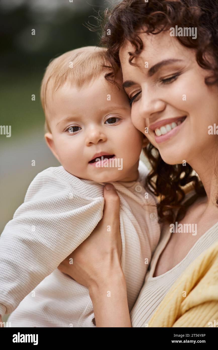 ritratto di una donna sorridente con occhi chiusi che abbraccia il bambino all'aperto, momenti felici Foto Stock