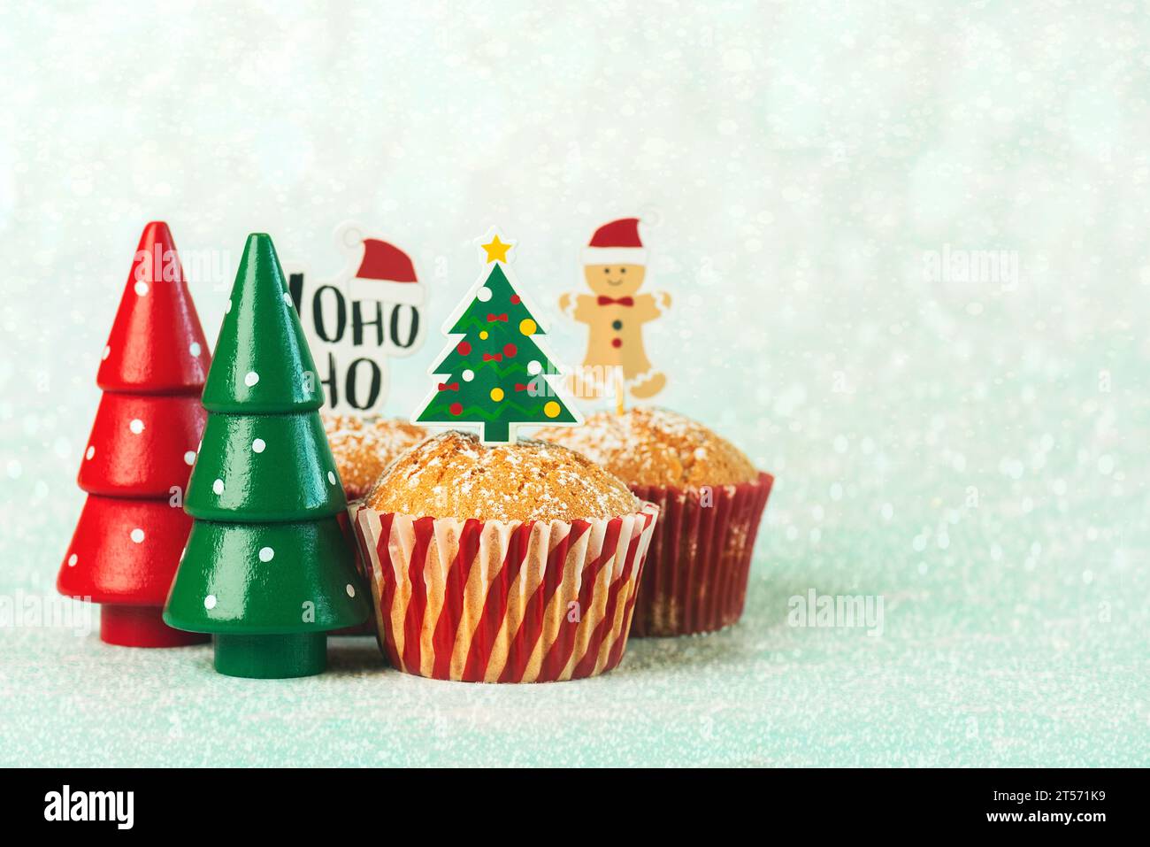 Muffin di natale fatti in casa con divertenti cartelli natalizi e alberi di natale su sfondo blu. Dolce concetto natalizio Foto Stock